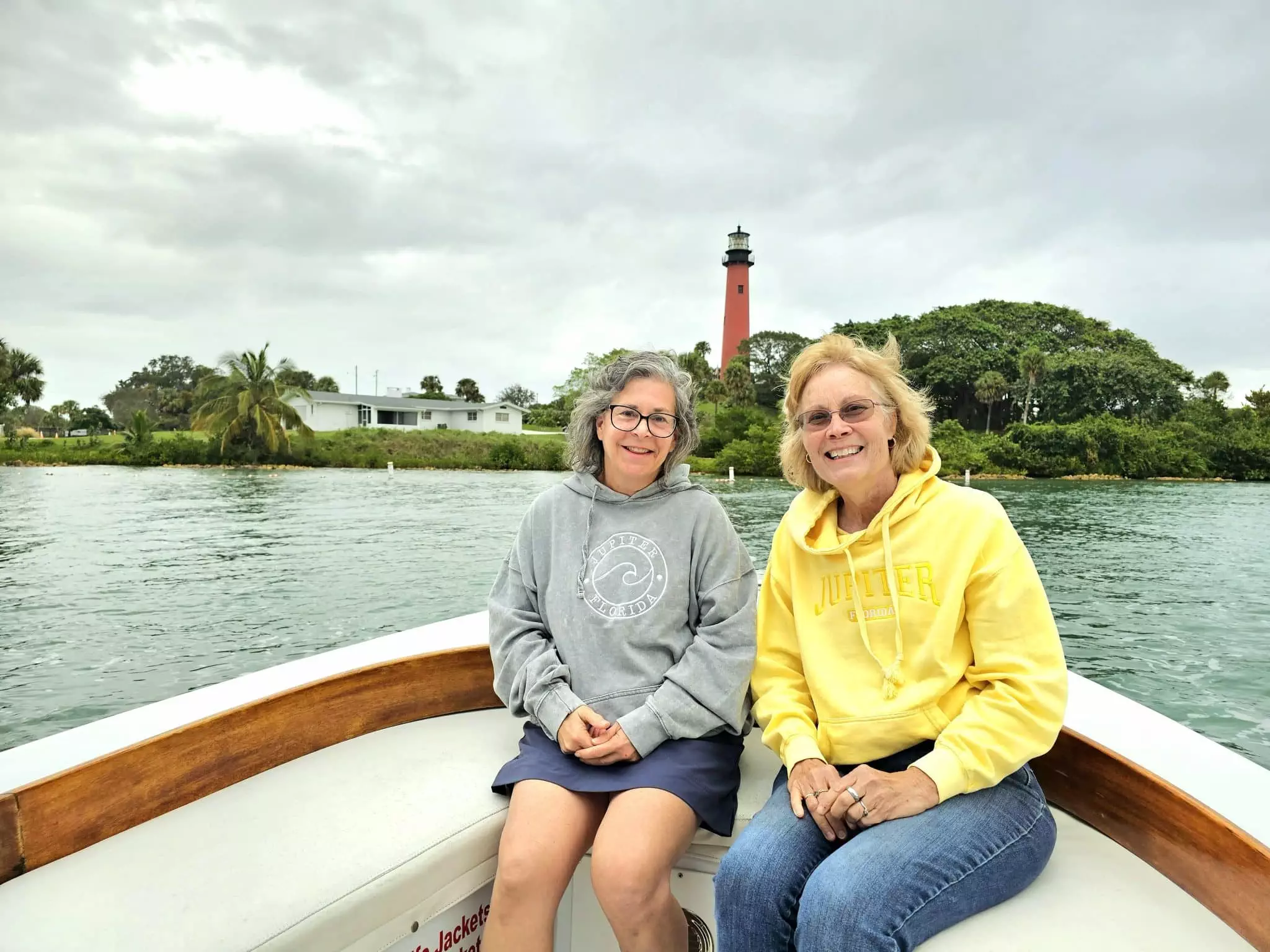 Two women enjoy a scenic holiday boat tour, sitting on a boat in front of a majestic lighthouse.