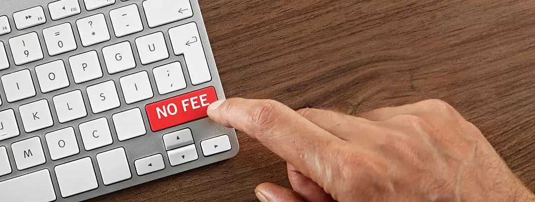 A hand pressing a red "NO FEE" key on a white computer keyboard on a wooden surface, reminiscent of booking an exclusive private boat tour with ease.